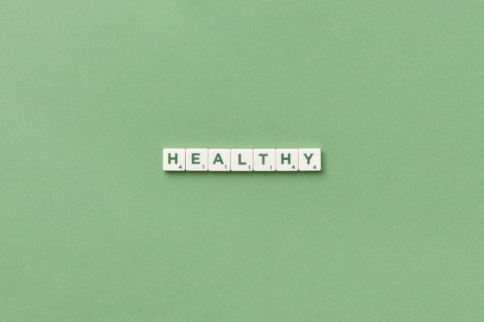 Scrabble tiles spelling the word 'healthy' on a light green background, top view. — Drug Discovery and Development Aligns Edu