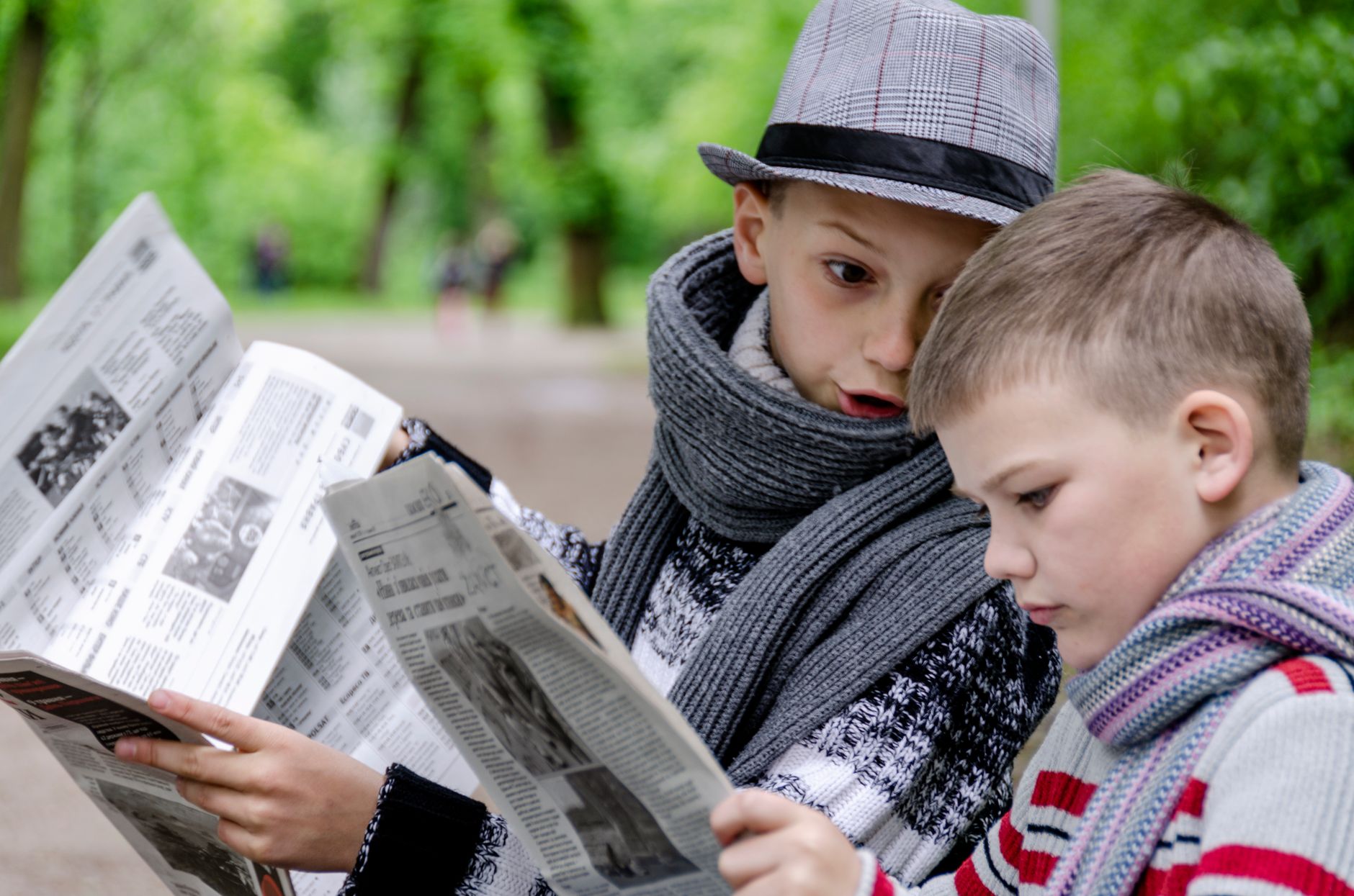 Two young boys reading newspapers together in a lush green park in Lviv, Ukraine. — Impair Technologies and SaaS