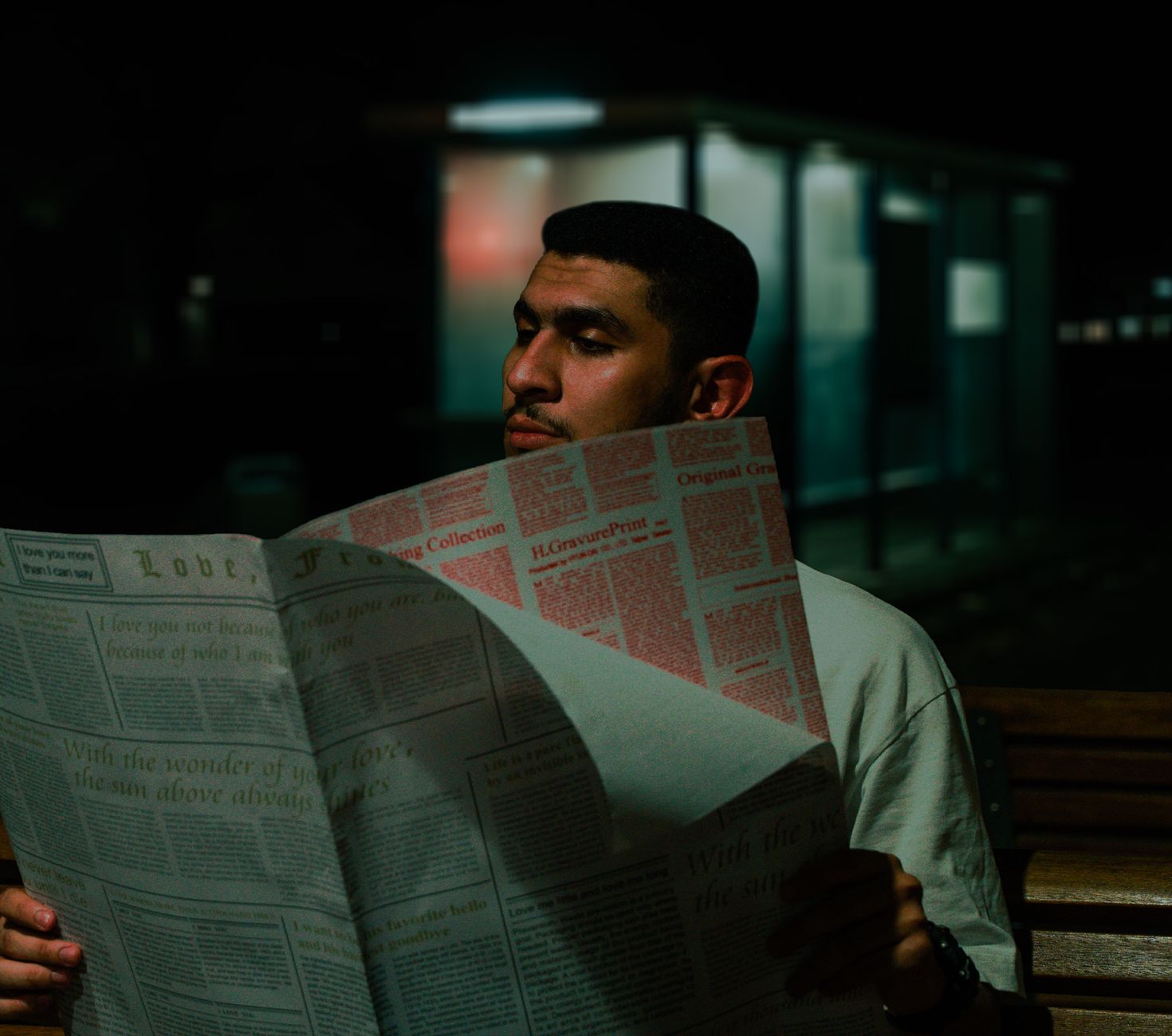 A man reads a newspaper at night on a bench, surrounded by urban darkness. — On the web Board Group meetings