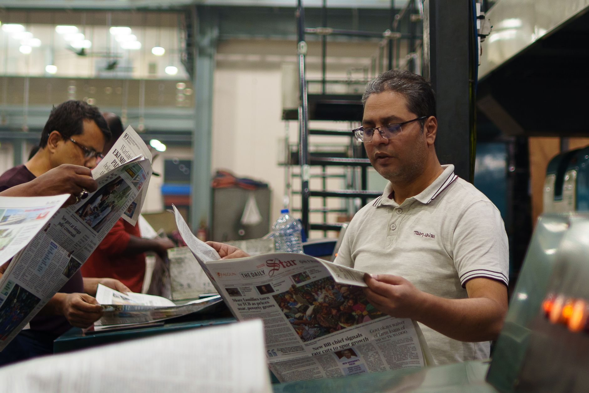 Workers at a newspaper printing press reading freshly printed copies. Focus on a man holding a newspaper. — Research Papers a