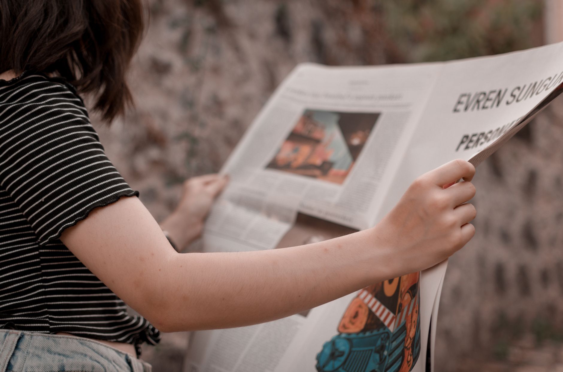 A woman holding a newspaper while sitting outside, enjoying a leisurely read. — Top online business Tools