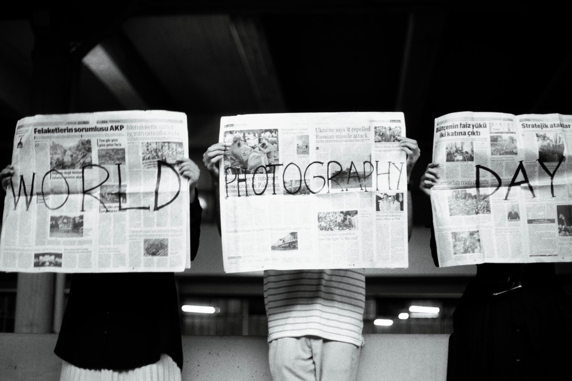 Three people hold newspapers with 'World Photography Day' text, artistic vibe. — Using a Electronic Studio to boost Your Onli